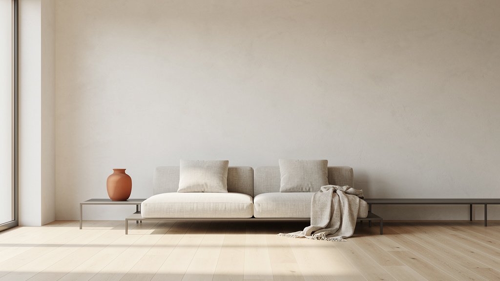 A wide, sunlit minimalist living room with an off-white plaster wall, a low linen sofa, a terracotta ceramic vase and ge